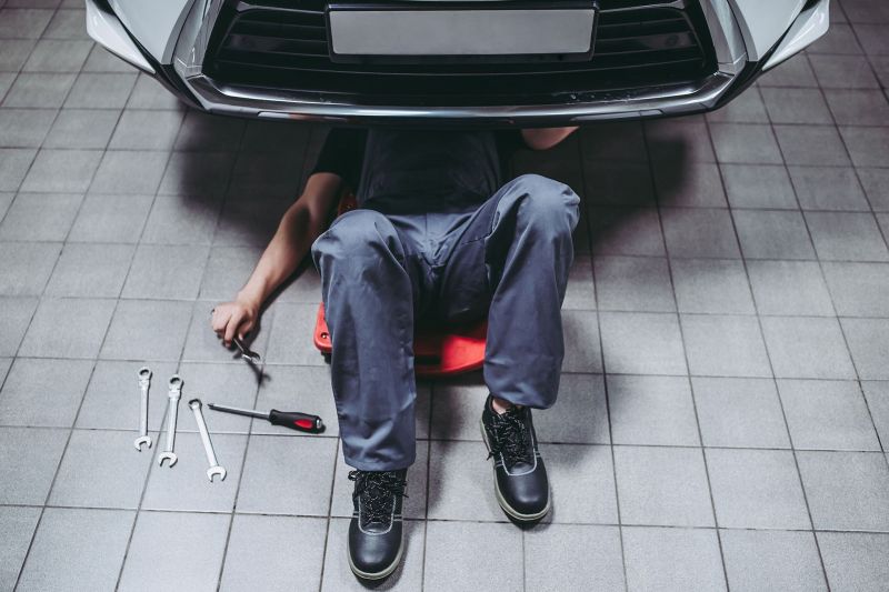 Mechaniker in Uniform liegt unter einem Auto und repariert dieses